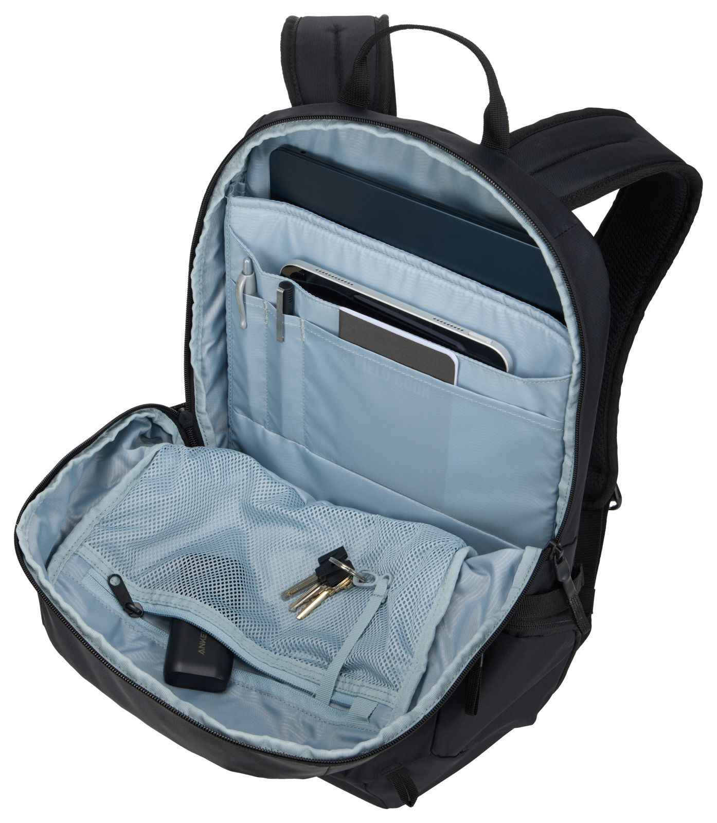 Zaino nero con scomparto principale aperto, contenente laptop, tablet, penne, chiavi e un power bank.