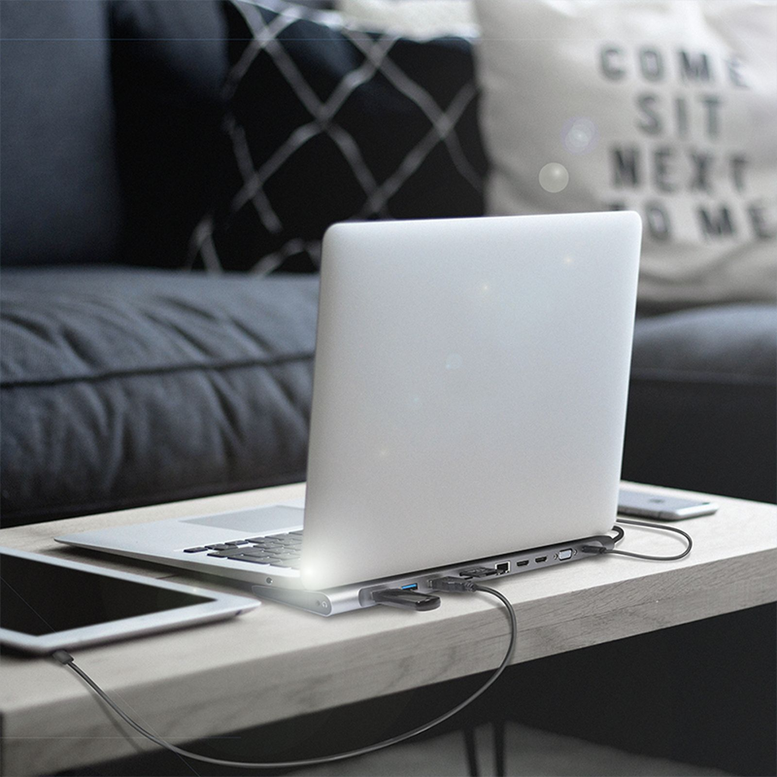 Ein Laptop auf einem Tisch mit einem USB-Hub, Tablet und Handy.