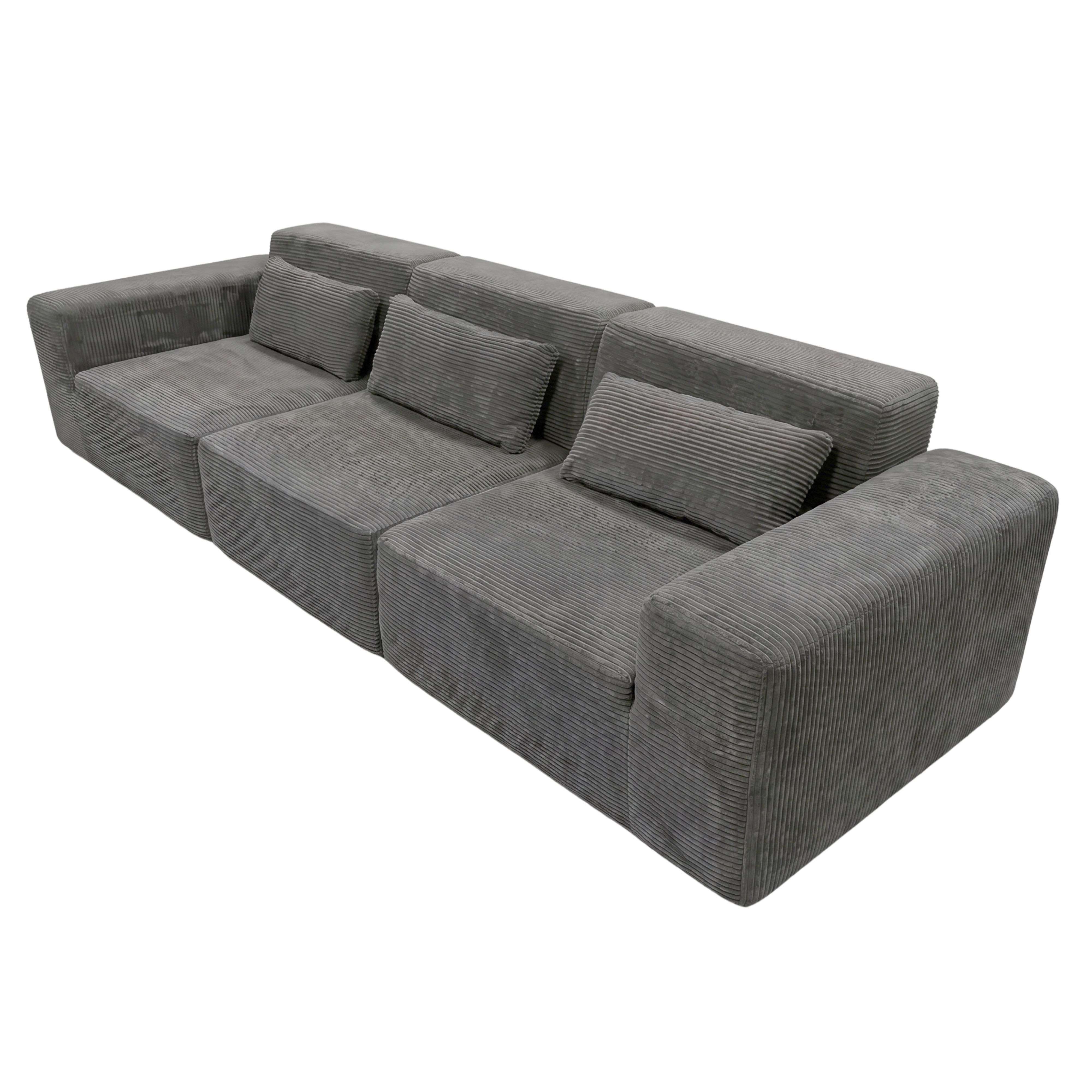 Sofá modular seccional gris de pana con cuatro asientos y tres cojines.