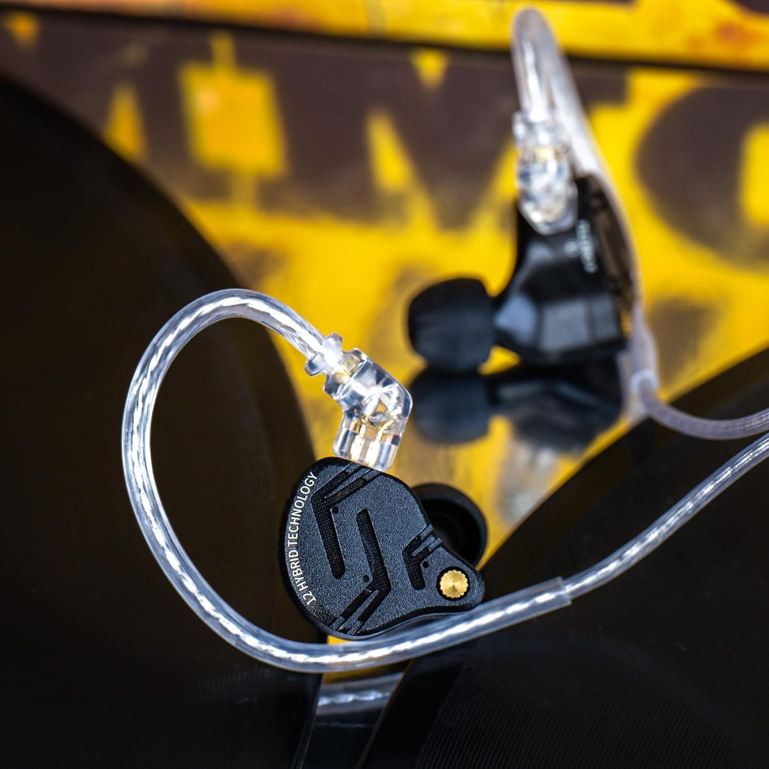 Moniteurs intra-auriculaires noirs avec fils transparents sur surface sombre avec fond jaune.