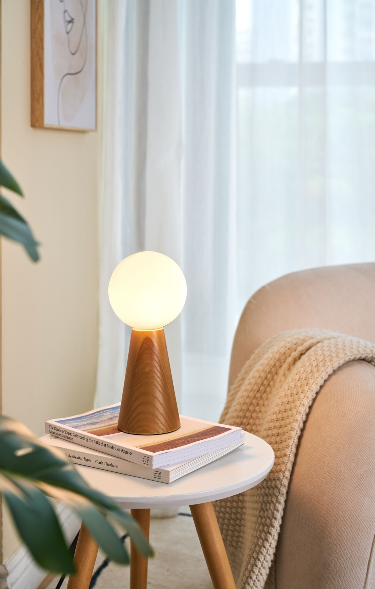 Ein Nachttisch mit Lampe, Büchern und einer Decke auf einem Sessel.