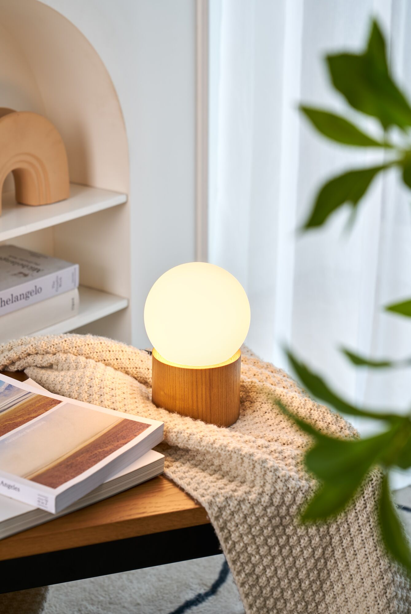 Eine Nachttischlampe mit Holzsockel und kugelförmigem Lampenschirm.