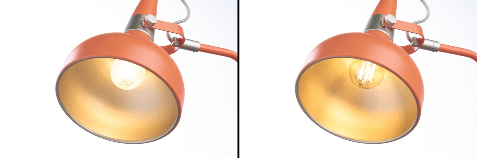 Eine orangefarbene Lampe mit einem goldenen Reflektor und einer Glühbirne.