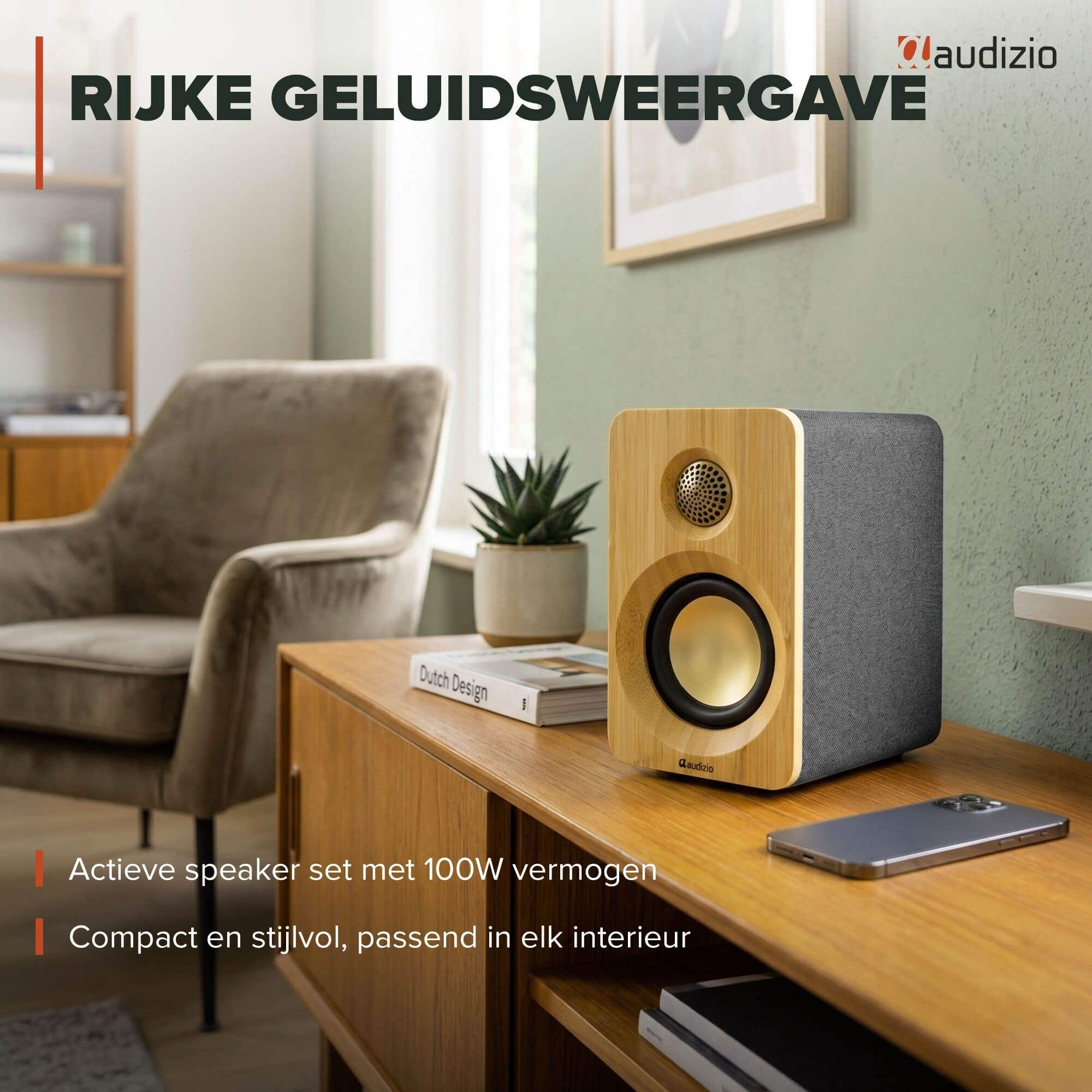 Un altavoz con frontal de madera y tela gris, junto a un libro y un teléfono.
