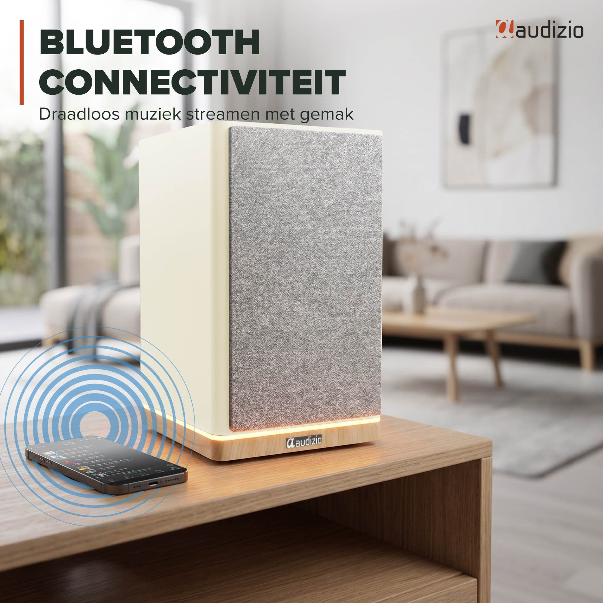 Un altavoz crema con frontal de tela está sobre una mesa de madera junto a un smartphone.