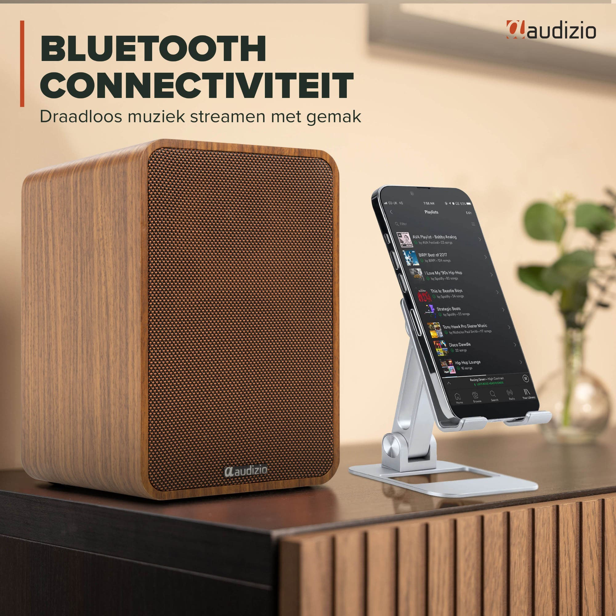 Altavoz de madera junto a un smartphone mostrando una lista de música en soporte plateado.