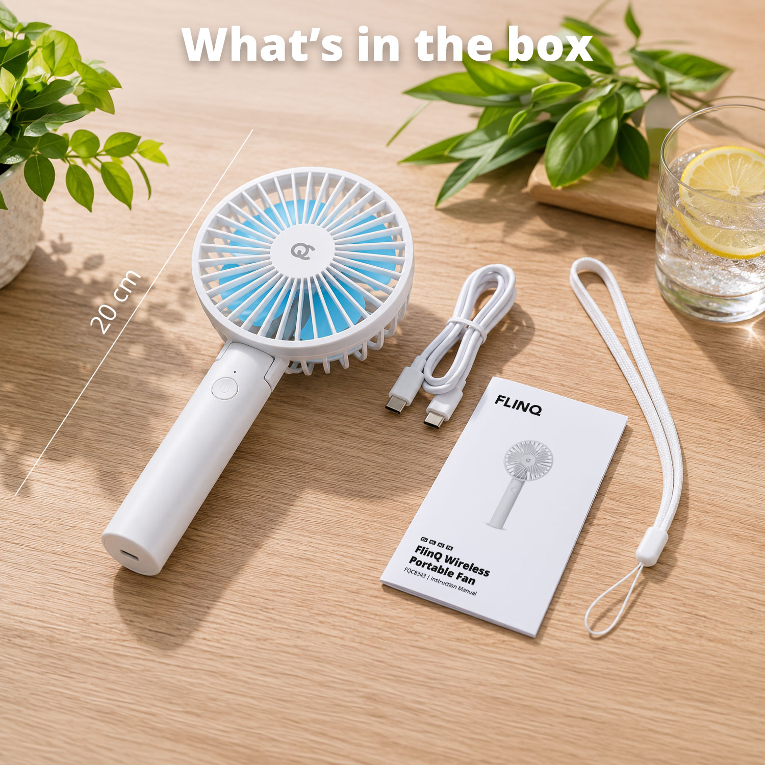 A white portable fan with blue blades, charging cable, and manual on a wooden surface.