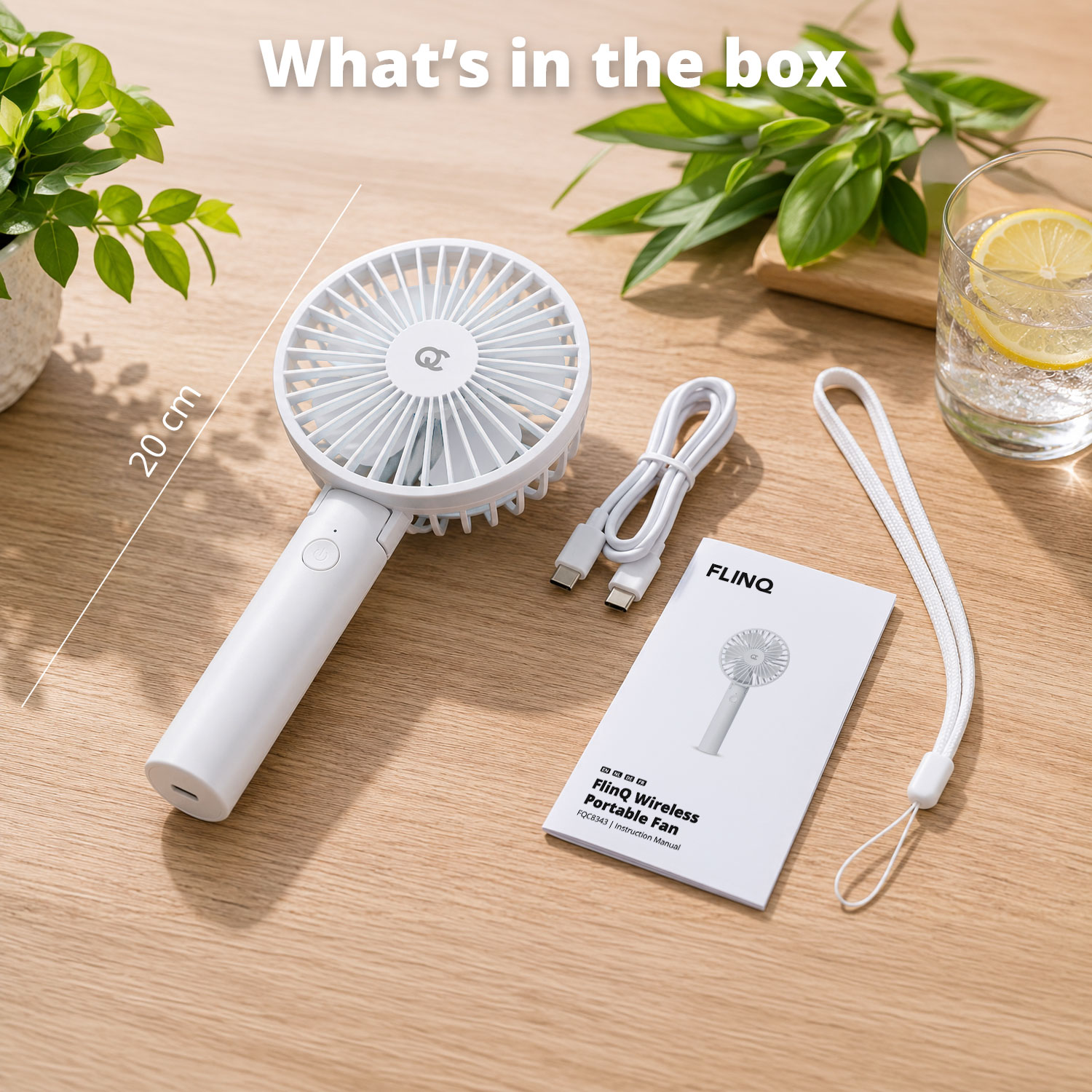 A white portable fan, cable, and manual lie on a wooden table.