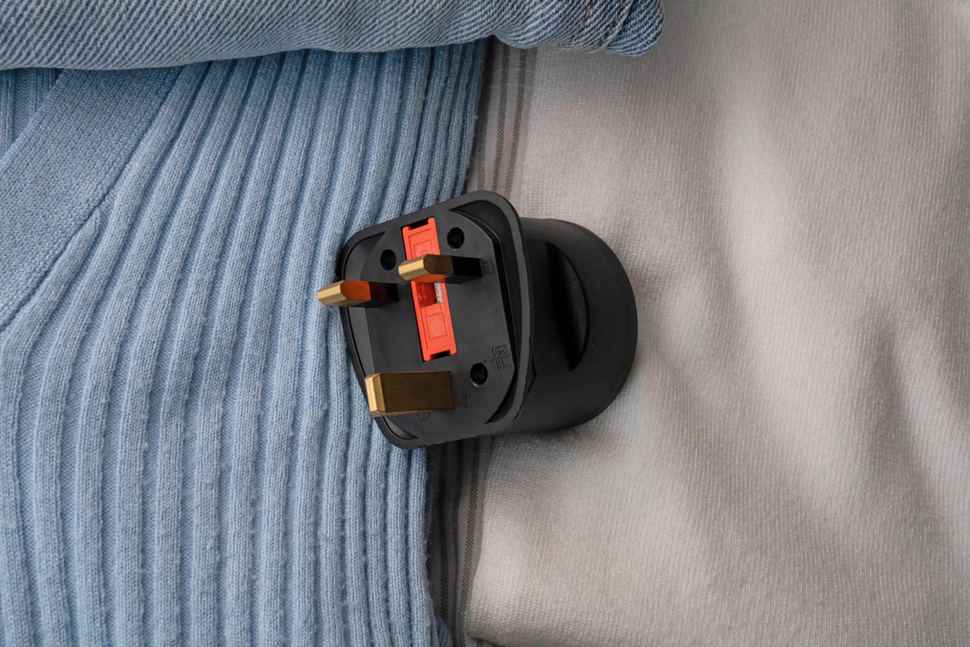 Un adattatore da viaggio nero con tre pin dorati e una leva arancione.