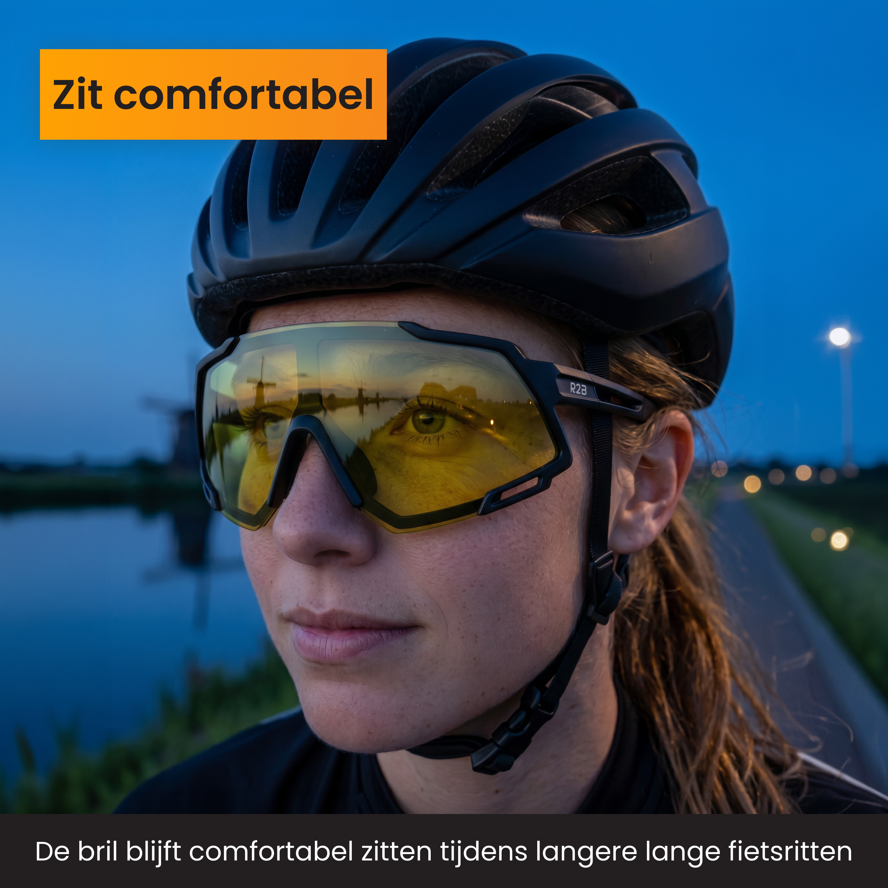 Radfahrerin mit gelben Brillen und Helm bei Dämmerung. Windmühle spiegelt sich in der Brille.