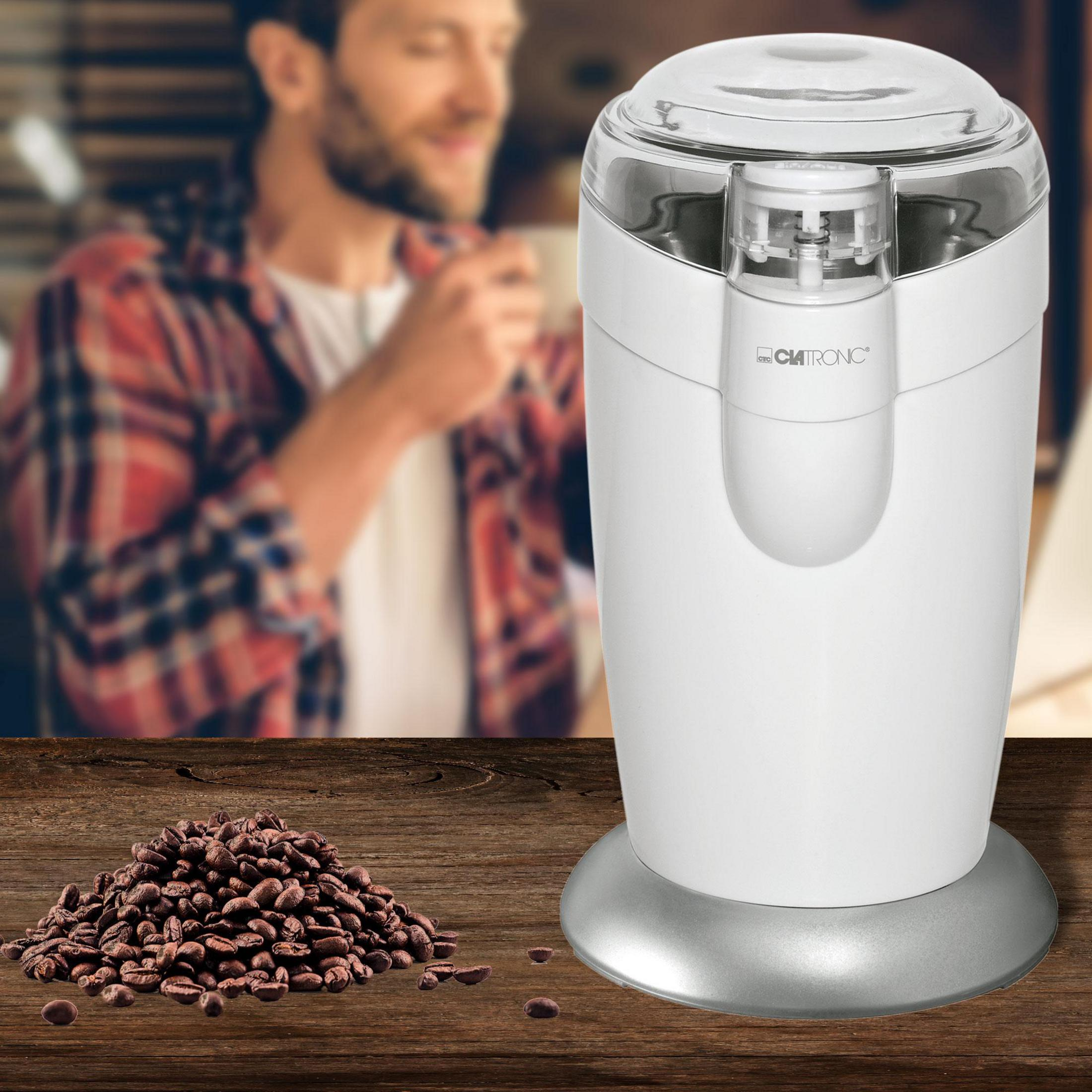 Un molinillo de café blanco junto a un montón de granos de café.