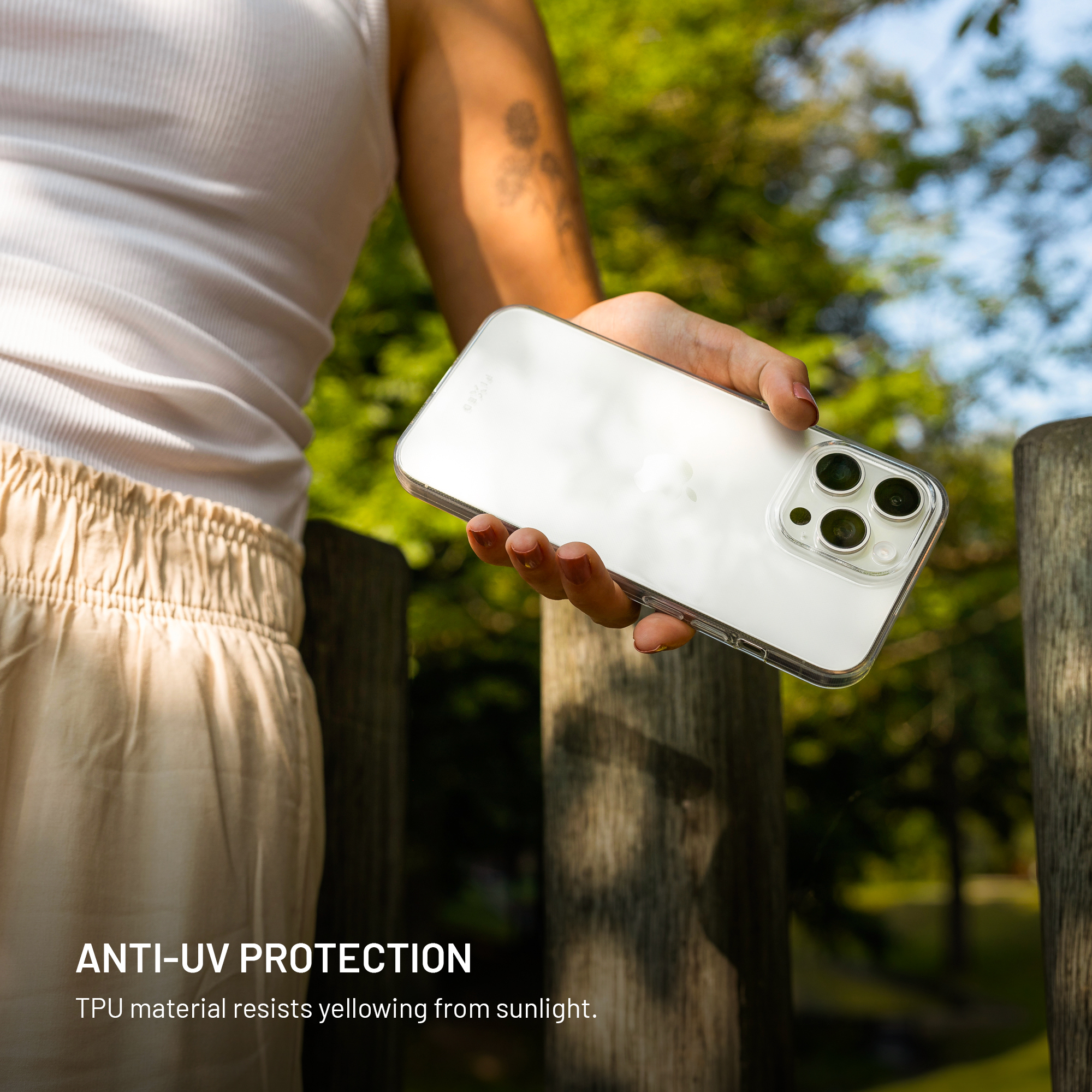 Eine Hand hält ein transparentes Handy vor einem unscharfen Hintergrund aus Bäumen und Holzpfosten.