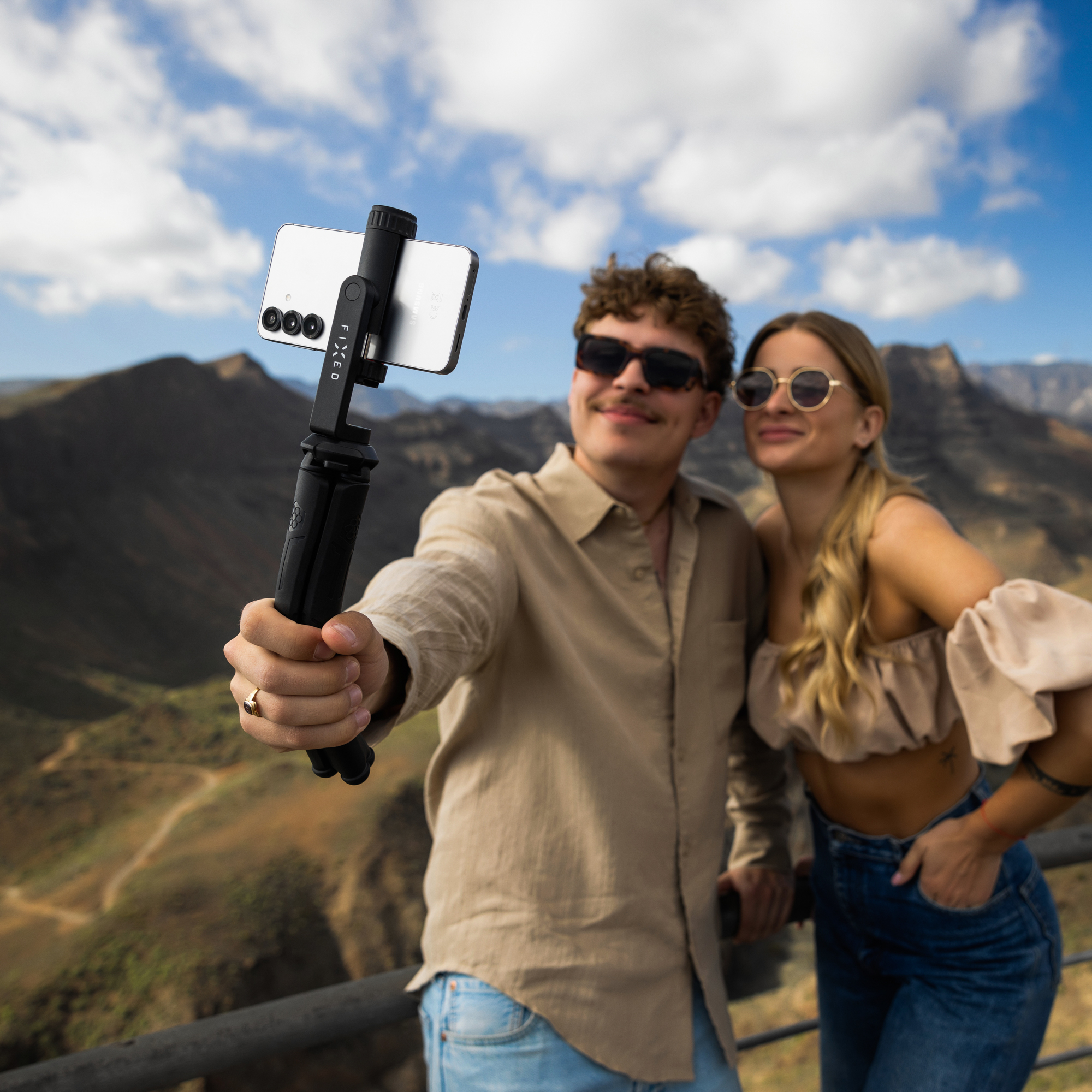 Mann und Frau machen Selfie mit Gimbal vor bergiger Landschaft.