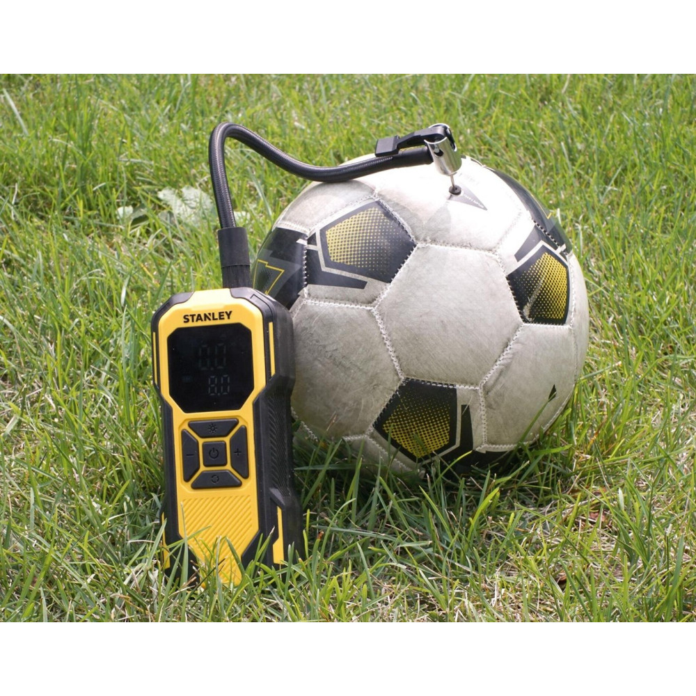 Un gonfiatore digitale Stanley giallo e nero collegato a un pallone da calcio sull'erba.