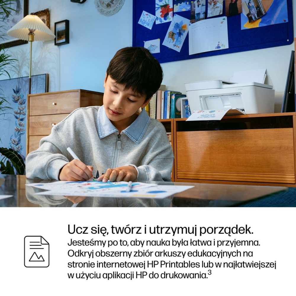 Chłopiec rysuje przy stole, w tle drukarka i tablica ogłoszeń.