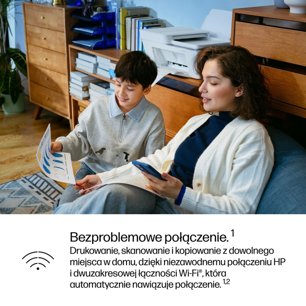 Kobieta i chłopiec siedzą, patrząc na papiery i telefon. W tle drukarka.