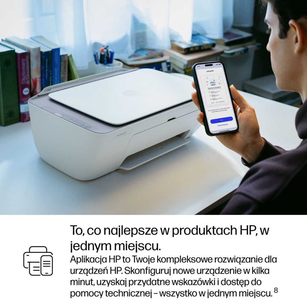 Mężczyzna trzyma smartfon przed drukarką HP. Książki w tle.
