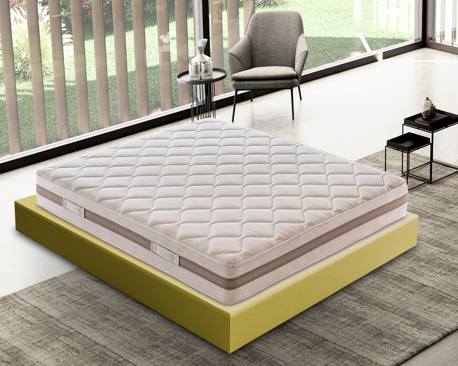 Un colchón blanco acolchado sobre una base de espuma amarilla, con sillón y mesa cerca.