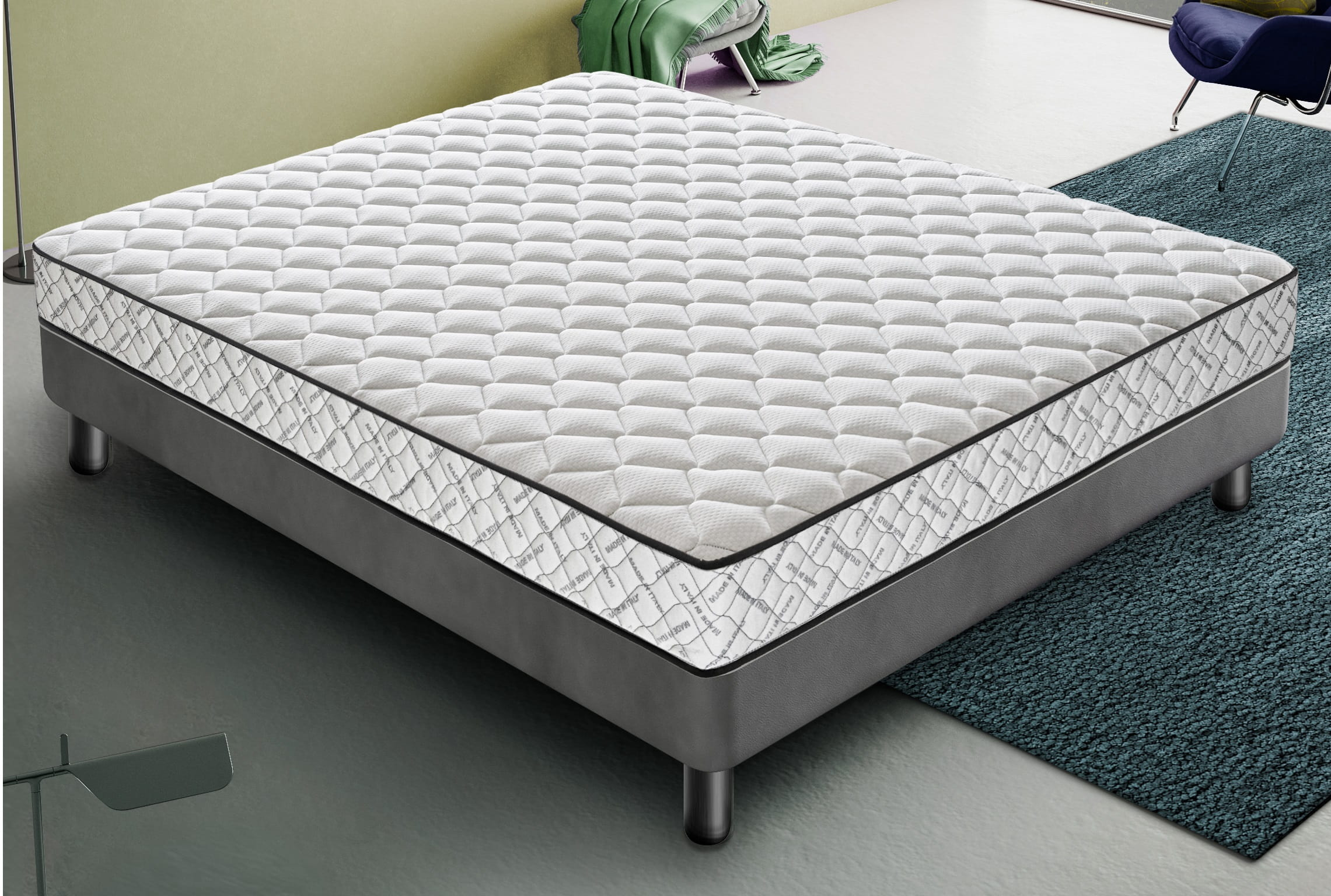 Un colchón blanco sobre una base gris con patas plateadas sobre una alfombra azul.