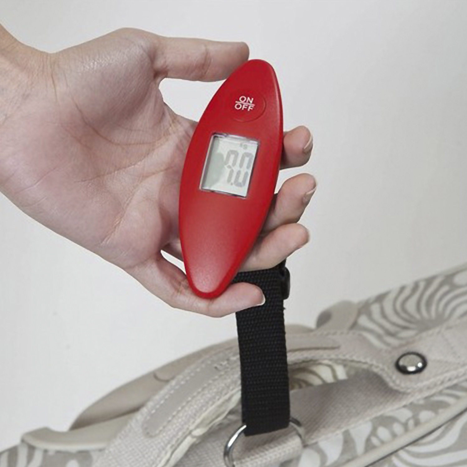 Una mano tiene una bilancia per bagagli rossa con display digitale che mostra 0.0.