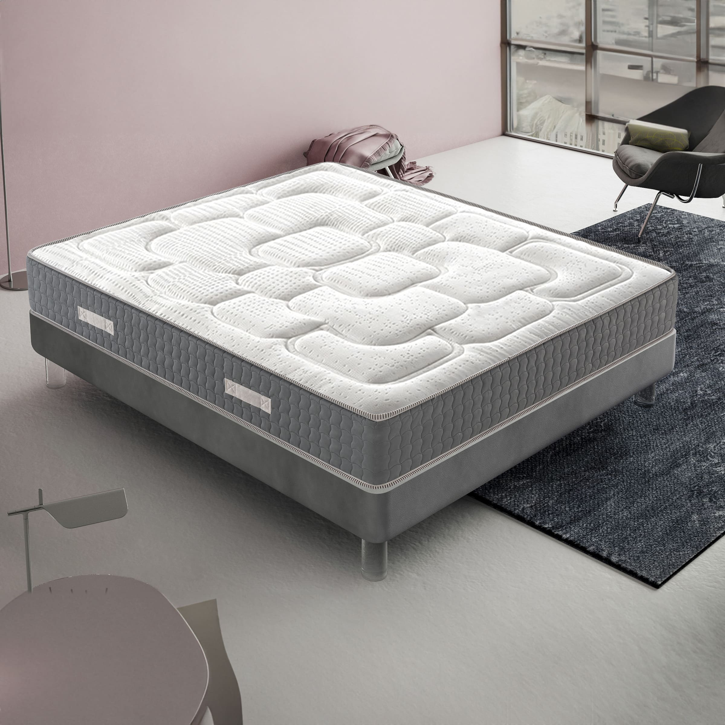 Una cama blanca y gris con colchón acolchado sobre una alfombra oscura.