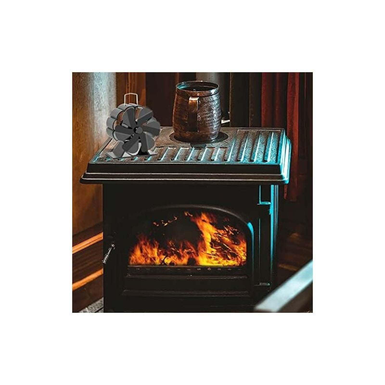 Ein schwarzer Holzofen mit brennendem Feuer und einem Lüfter darauf.