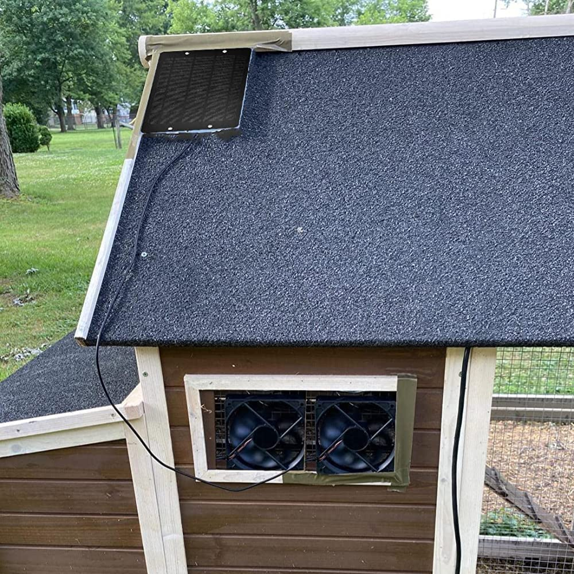 Ein Hühnerstall mit zwei Lüftern in einem Fenster und einem Lüftungsgitter auf dem Dach.