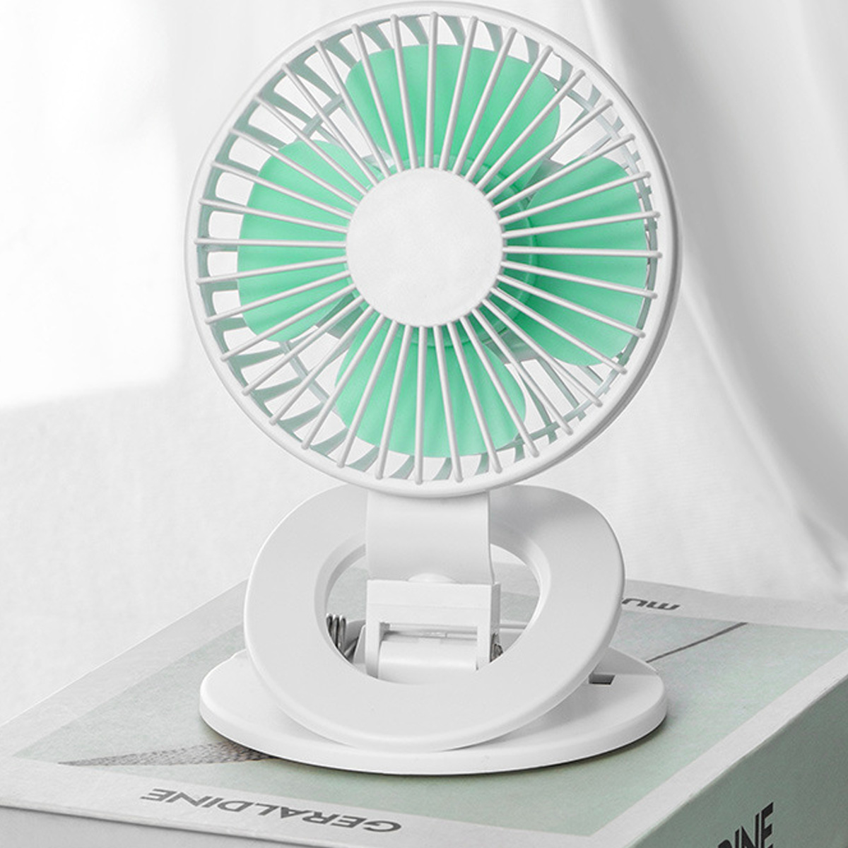 Ein kleiner weißer Ventilator mit grünen Flügeln steht auf einem Buch.