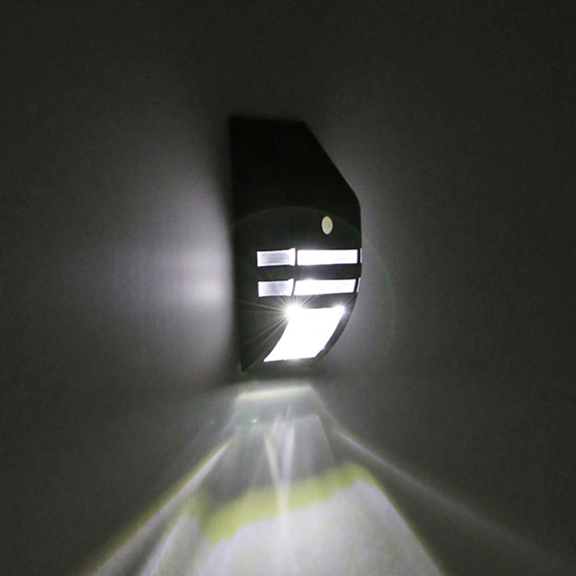 Ein schwarzer Wandstrahler beleuchtet eine Wand mit Lichtstrahlen.