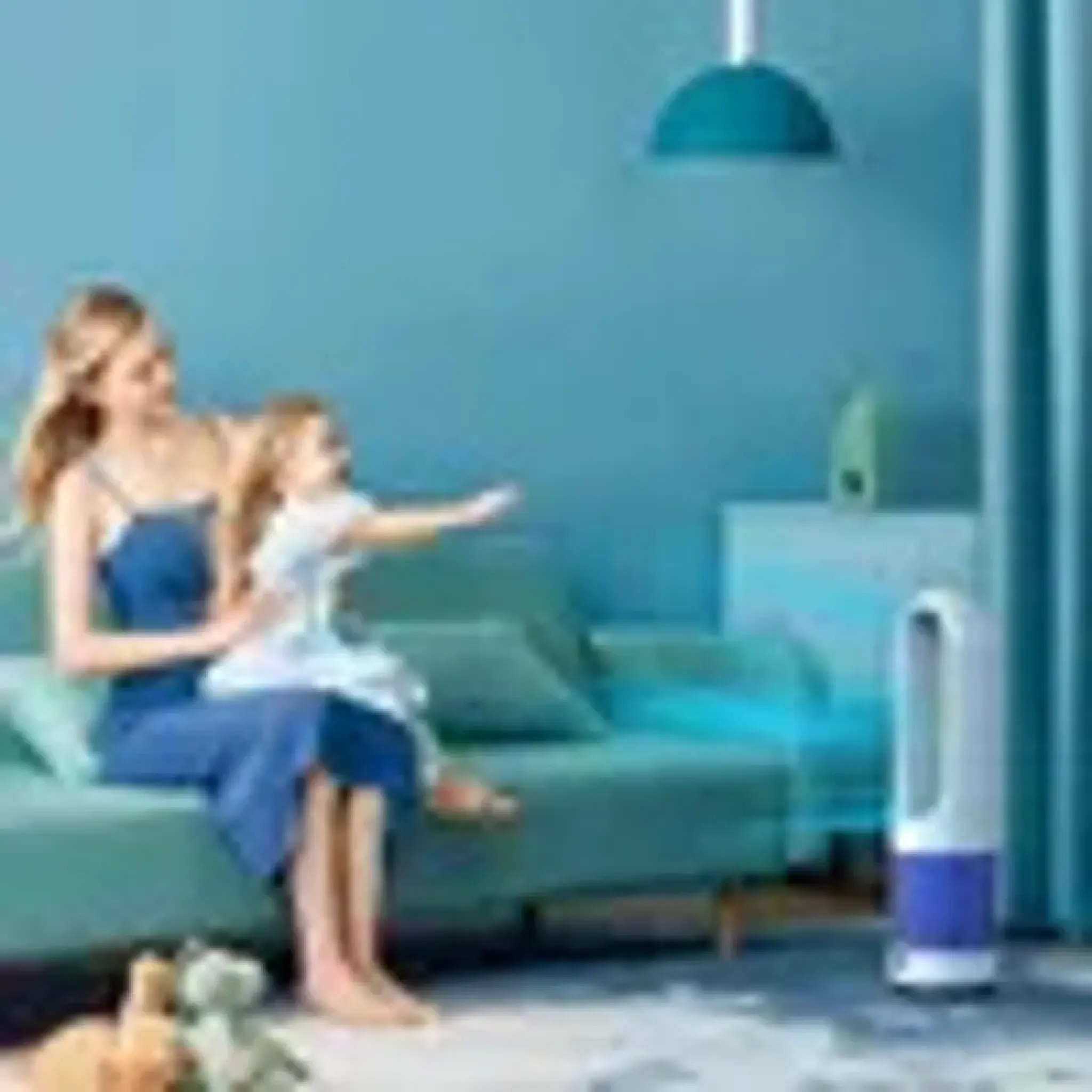 Eine Frau und ein Kind sitzen auf einem Sofa, ein Ventilator läuft.