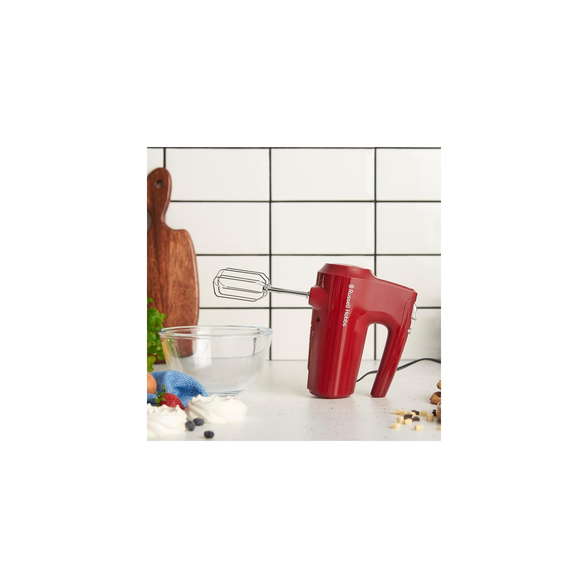 Ein roter Handmixer steht auf einer Arbeitsplatte neben einer Schüssel und Backzutaten.