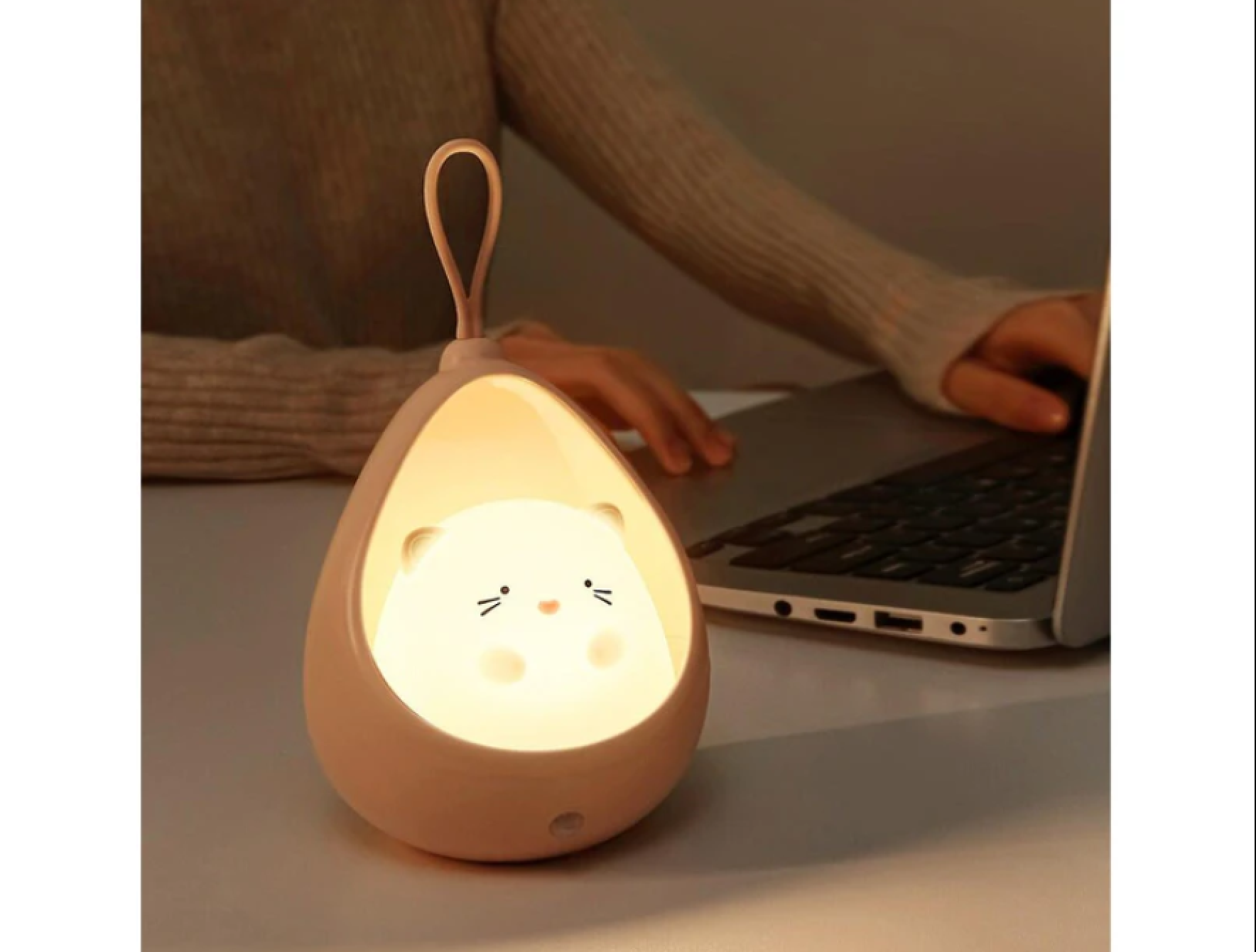Ein rosa Nachtlicht in Form einer Katze leuchtet auf einem Schreibtisch neben einem Laptop.