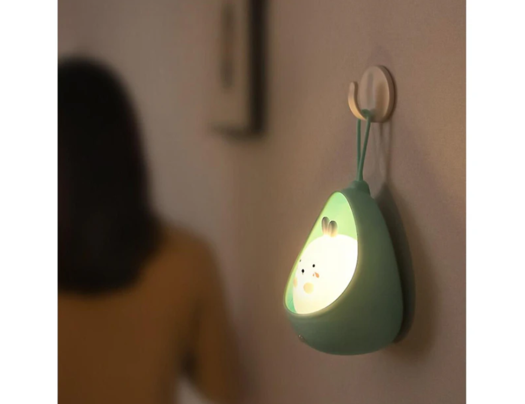 Ein grünes Nachtlicht in Avocadoform mit Hasenmotiv hängt an einer Wand.