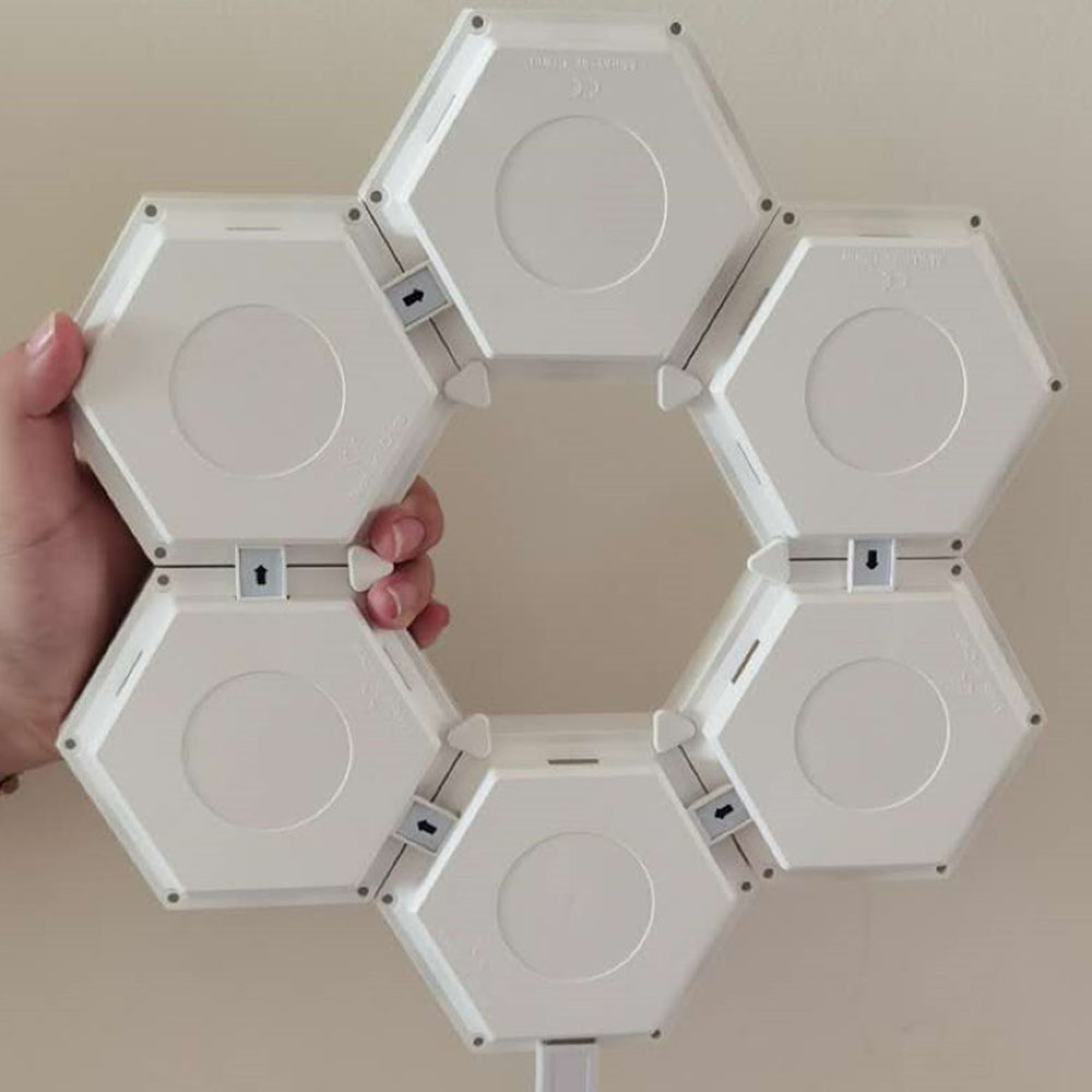 Sechs weiße sechseckige Module sind zu einem Ring verbunden. Eine Hand hält sie.