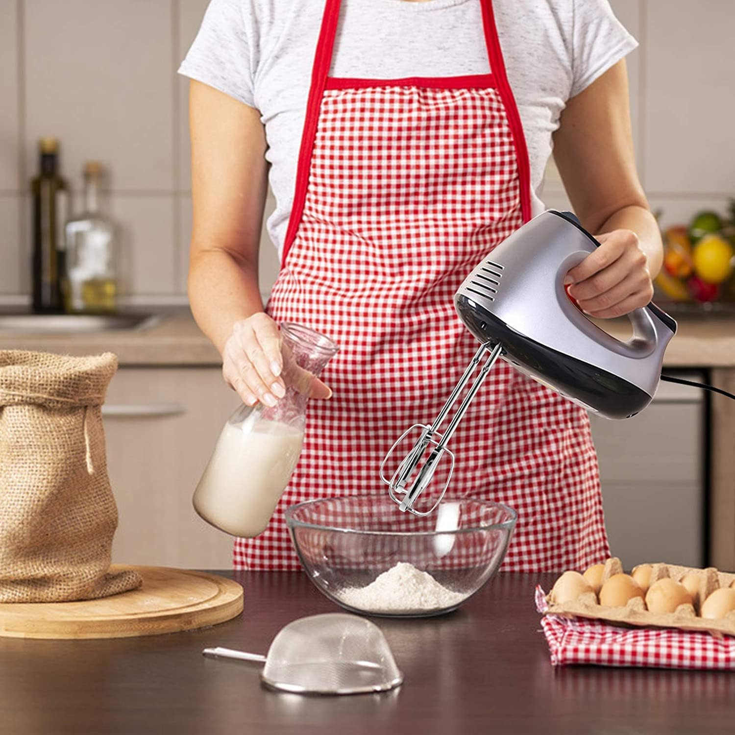 Eine Person in einer Schürze fügt Milch zu Mehl in einer Schüssel hinzu, um zu backen.