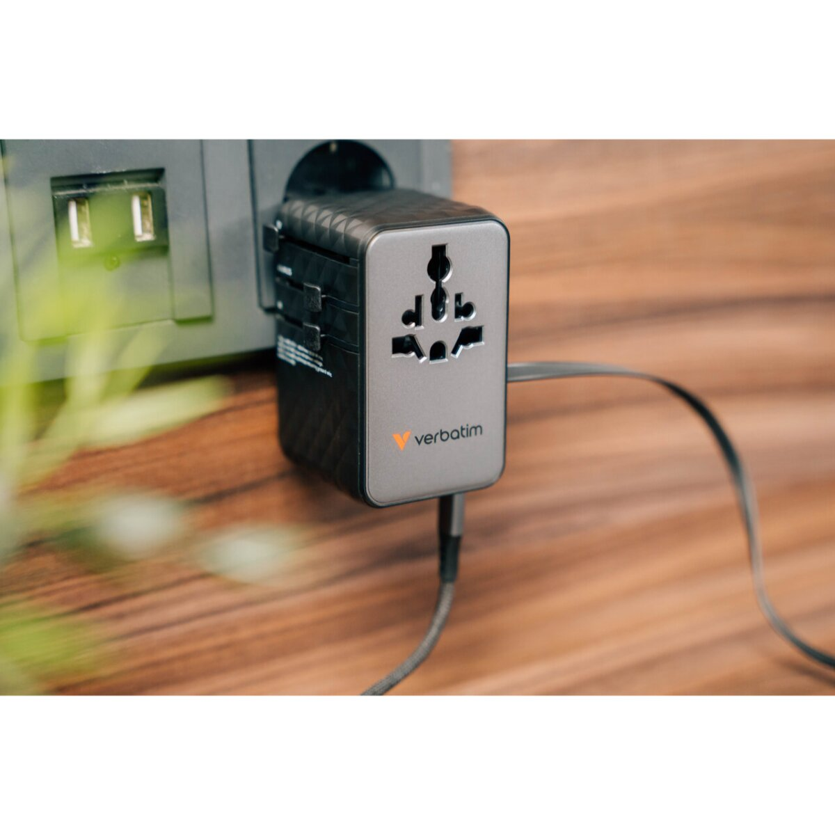 Un adattatore da viaggio Verbatim inserito in una presa a muro, collegato a un cavo USB.