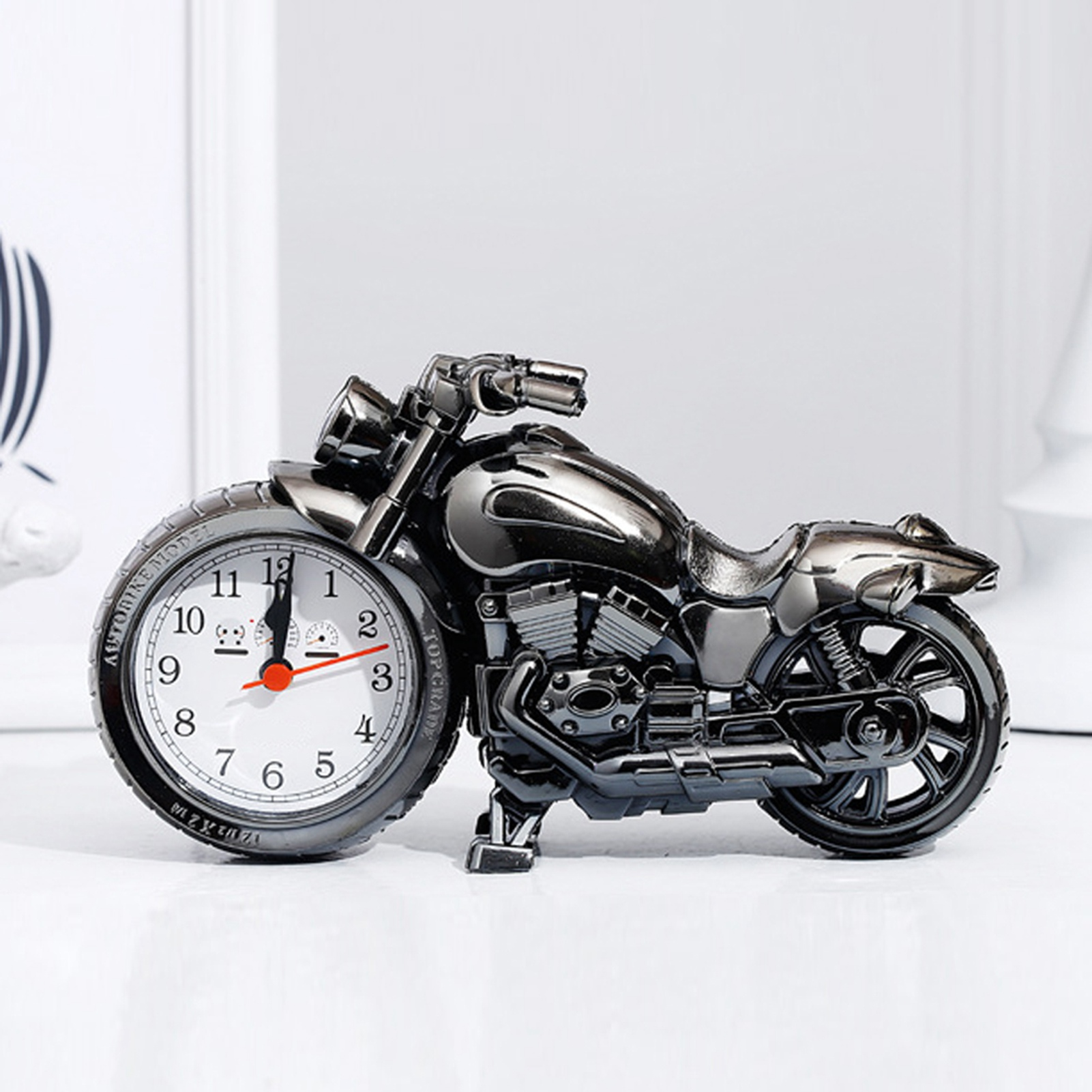 Ein metallfarbener Motorrad-Wecker mit weißem Zifferblatt und roten Zeigern.