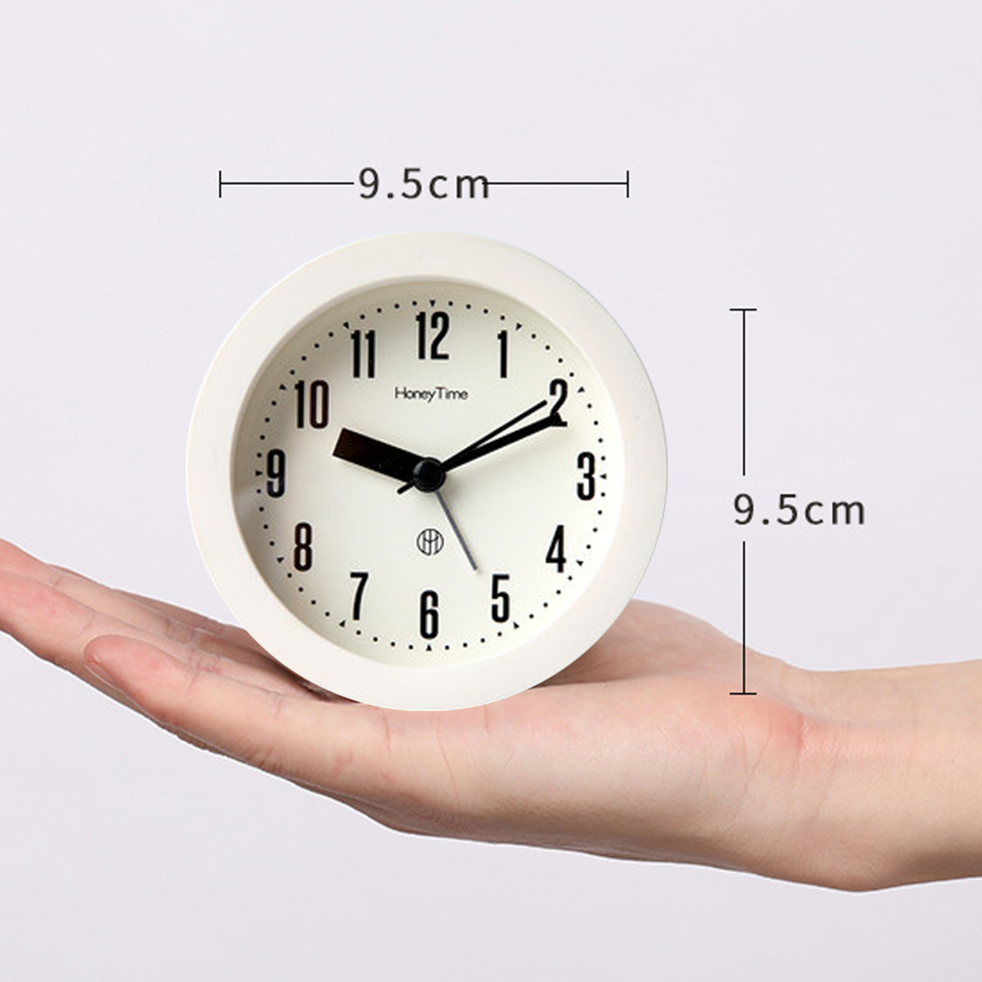 Eine weiße Weckeruhr mit schwarzen Ziffern liegt in einer Hand. 9,5 cm.