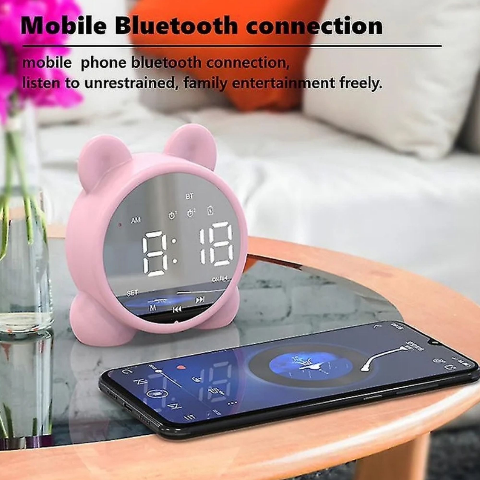 Ein rosafarbener Wecker mit Ohren und ein Smartphone auf einem Tisch.