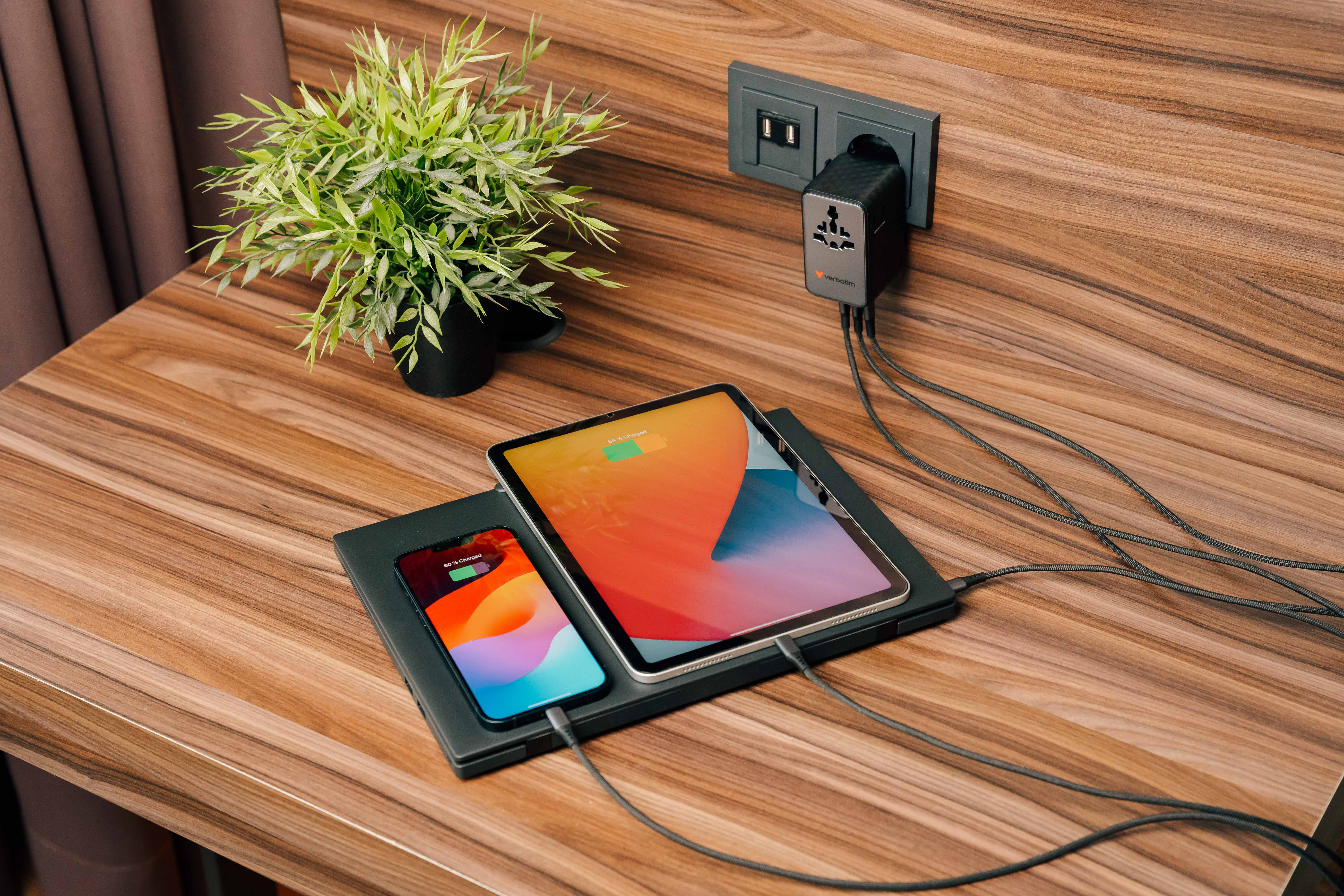 Une tablette et un téléphone se chargent sur un chargeur sans fil. Une plante est à proximité.