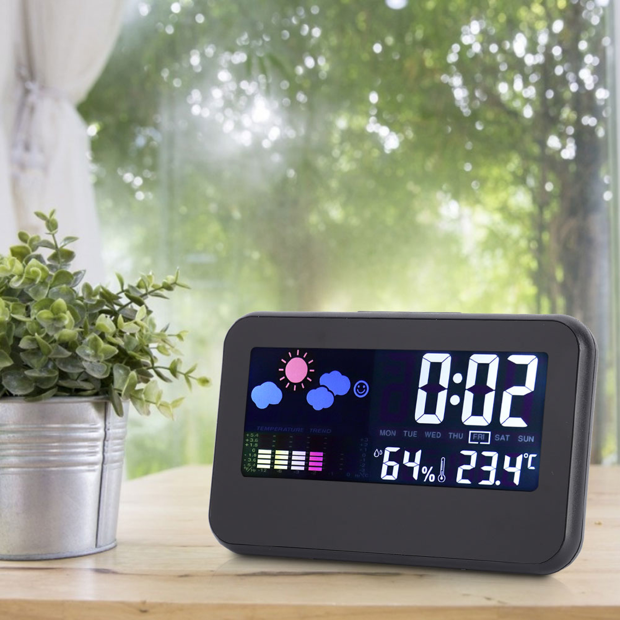 Ein digitaler Wecker mit Wetteranzeige steht auf einem Holztisch neben einer Topfpflanze.