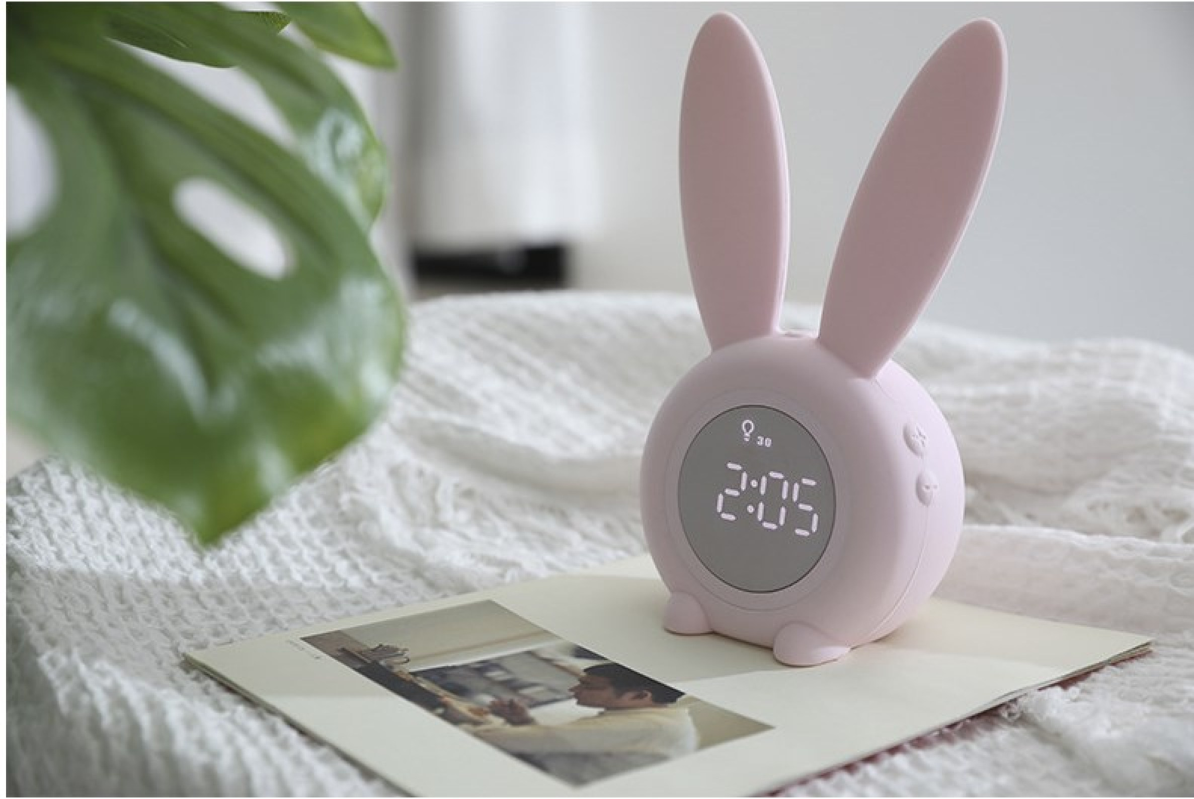 Ein rosafarbener Hase-Wecker mit digitaler Anzeige steht auf einem Buch.