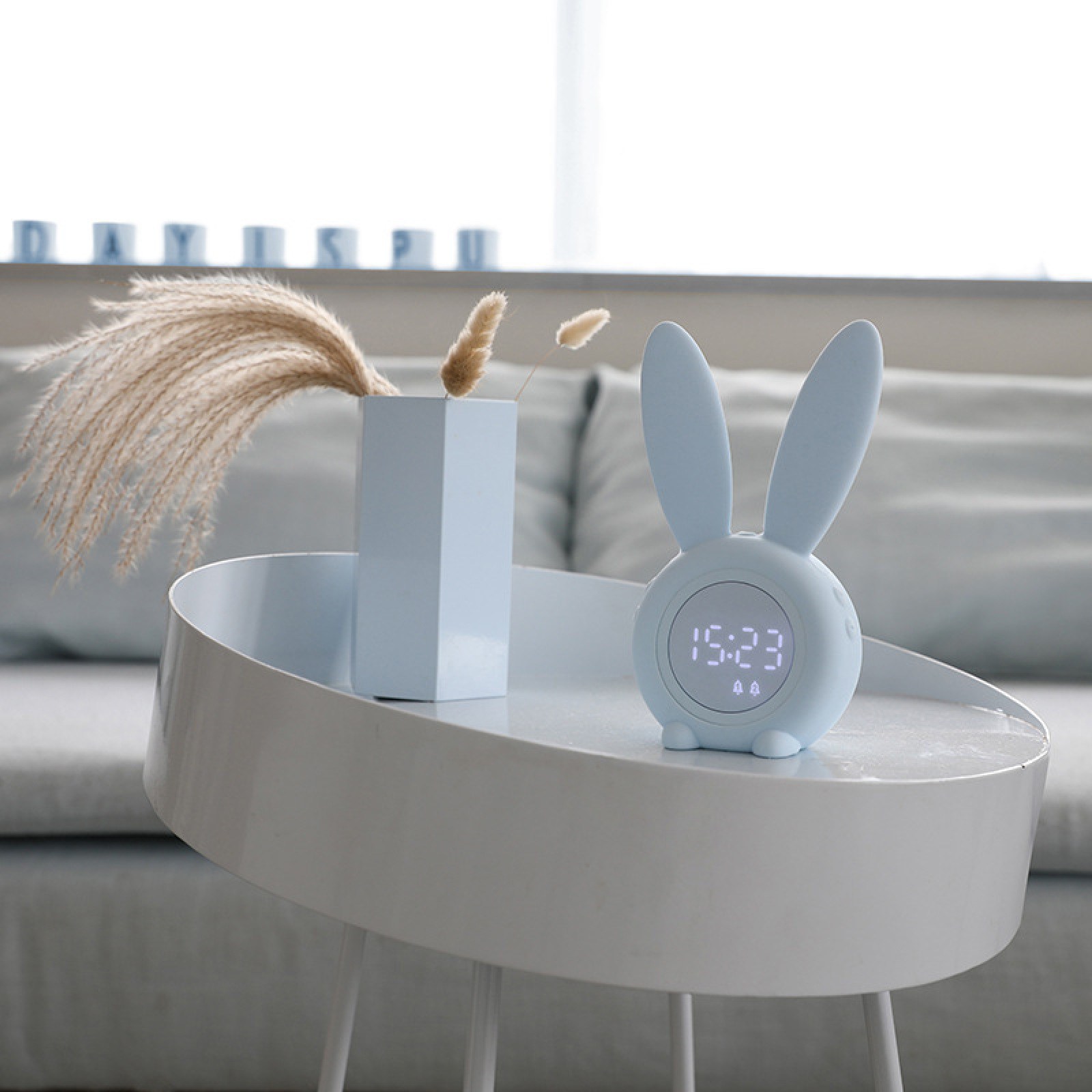 Ein blauer Hase-Wecker auf einem Tisch mit Vase und Pflanzen.