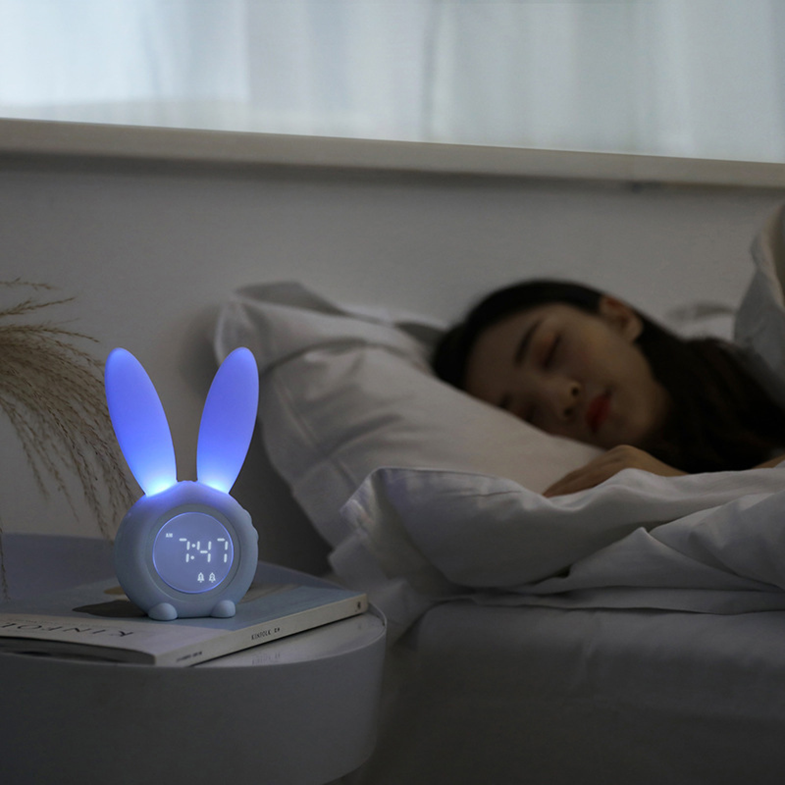 Ein Kaninchen-Nachtlicht mit digitaler Uhr steht neben einer schlafenden Person im Bett.