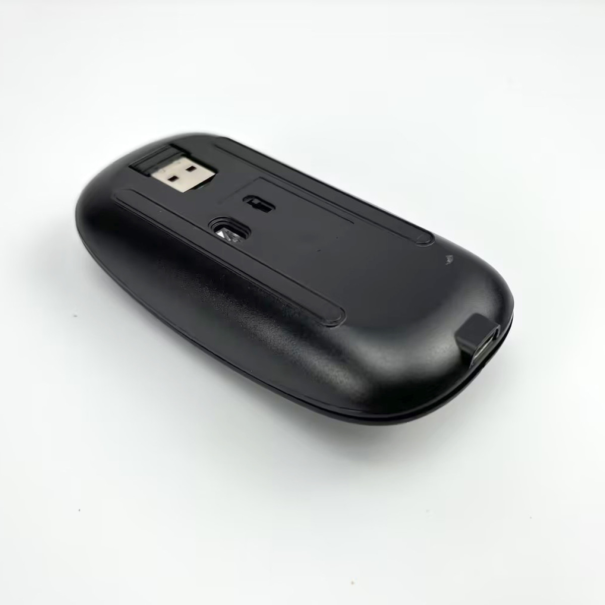 Unterseite einer schwarzen Computermaus mit USB-Empfänger und optischem Sensor.