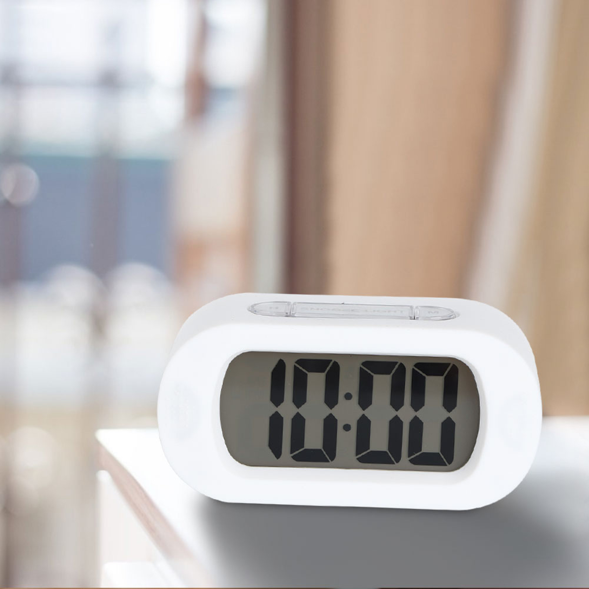 Ein weißer digitaler Wecker zeigt 10:00 an, steht auf einem Tisch.