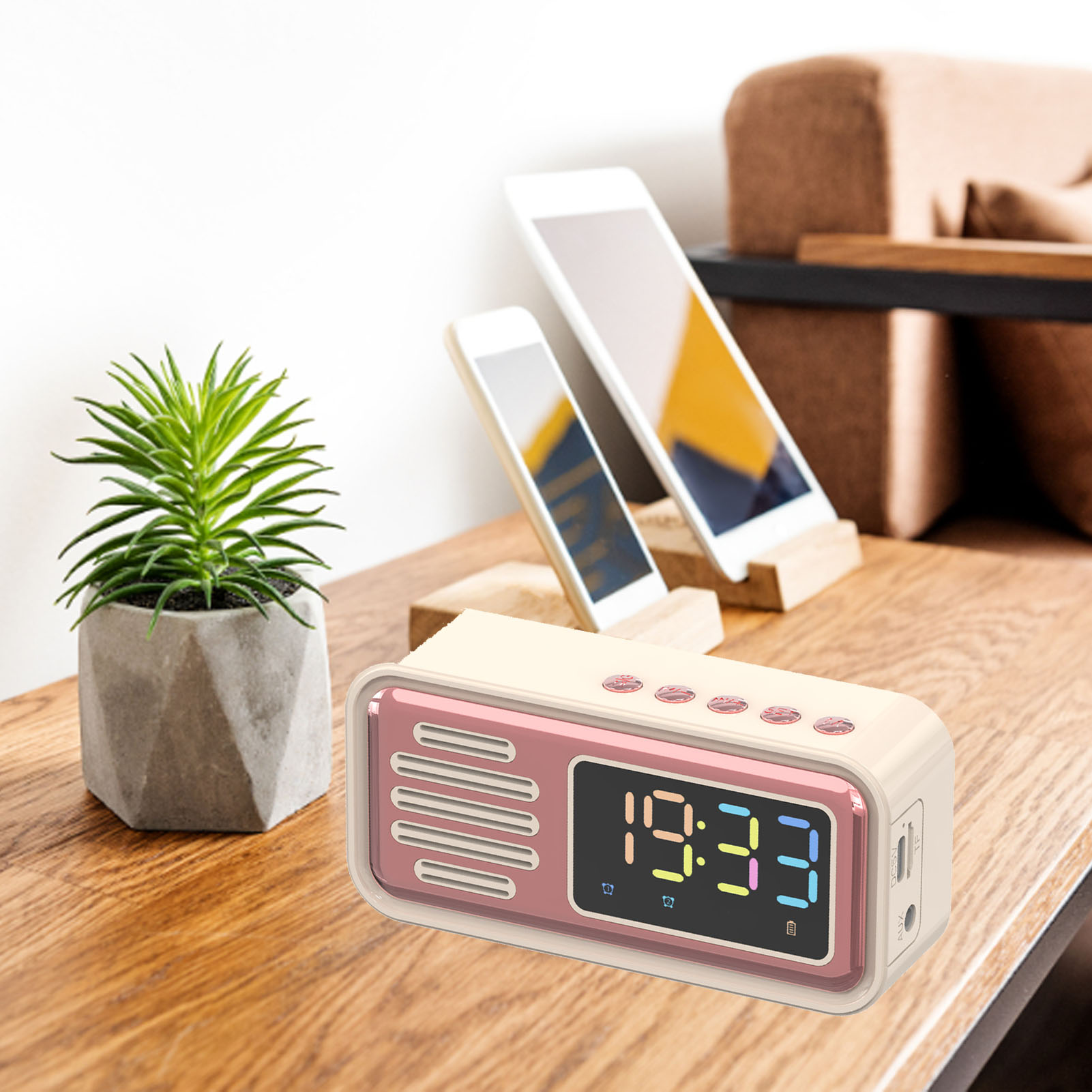Ein rosa und cremefarbener Lautsprecher mit Digitaluhr steht auf einem Holztisch neben einer Topfpflanze.