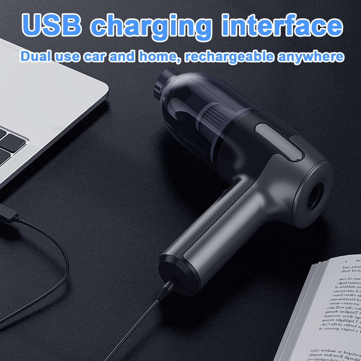 Ein schwarzer Handstaubsauger mit USB-Kabel lädt neben einem Laptop und einem Buch.