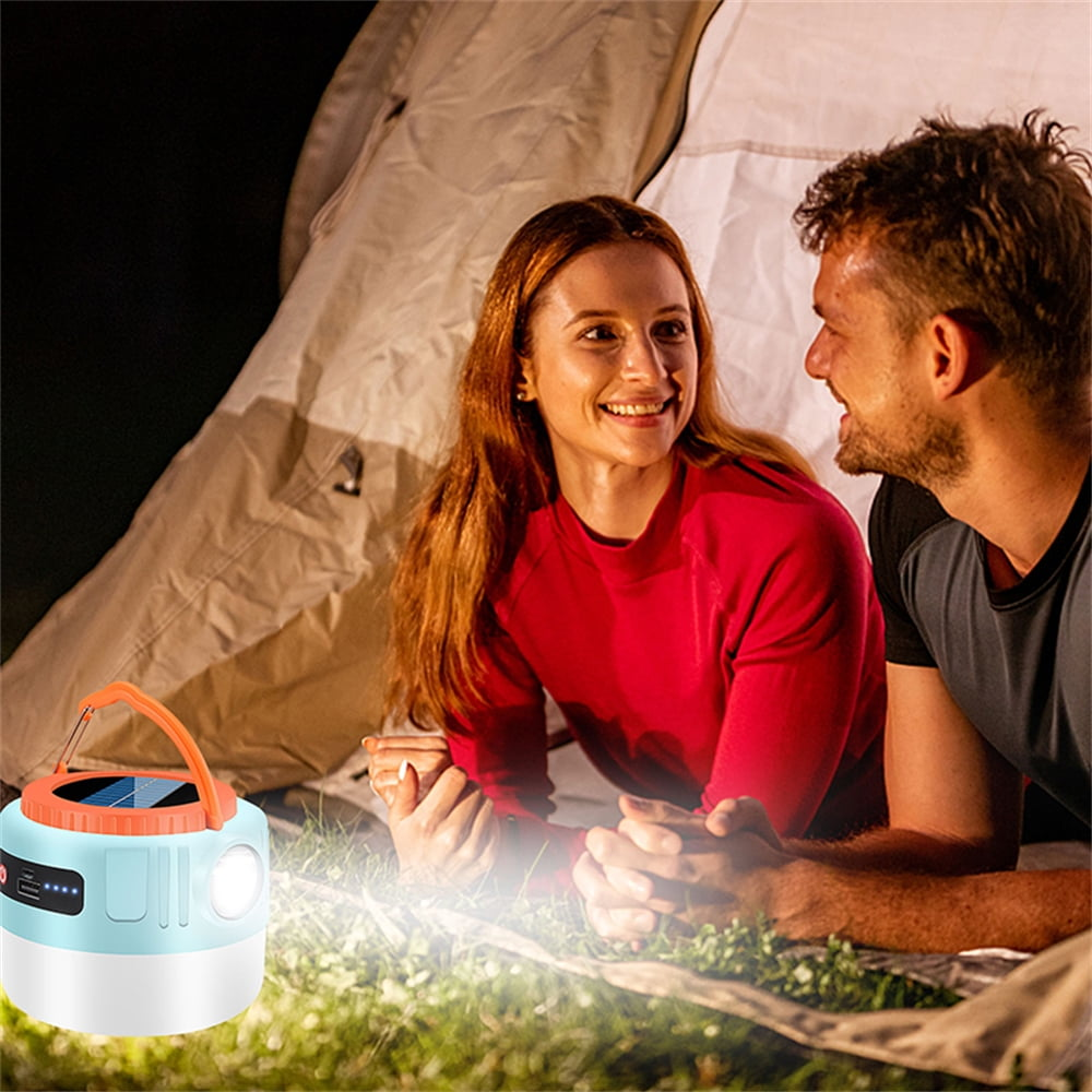 Ein Paar liegt vor einem Zelt, eine helle Lampe leuchtet.