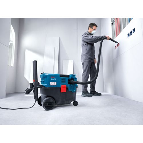 Mann mit Staubmaske saugt Wand mit Industriestaubsauger ab.